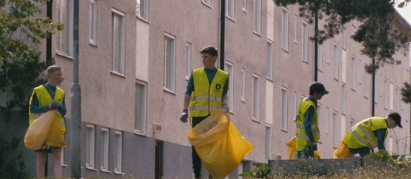 Ungdomar i varselvästar med gula soppåsar som plockar skräp utomhus