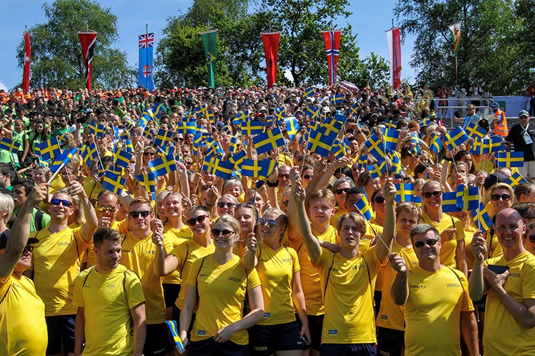 Folkhav med personer i sverigetröjor längst fram, viftandes med svenska flaggor.