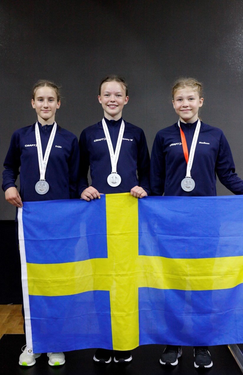 Tre svenska damjuniorer med silvermedaljer hållandes i svenska flaggan