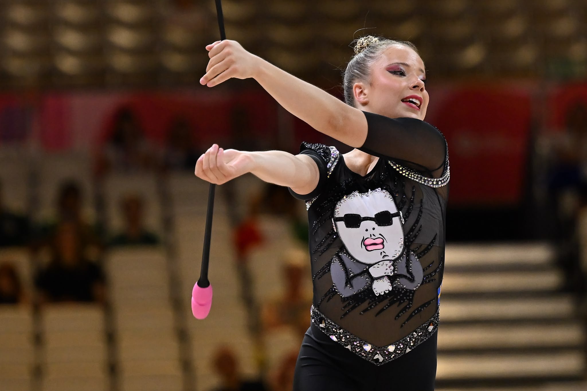 Gymnast i svart dräkt med en figur på framsidan. Håller i två käglor.